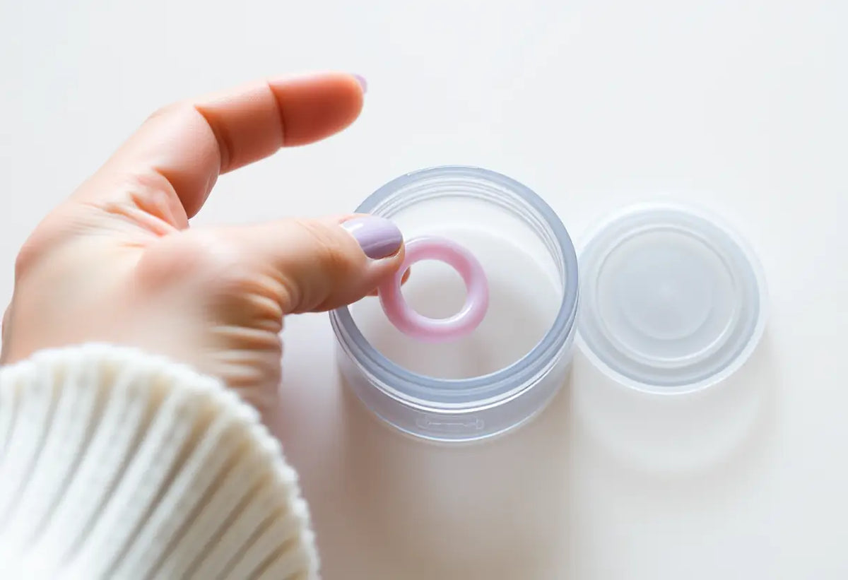 Une main féminine place un petit anneau en caoutchouc dans un contenant en plastique transparent