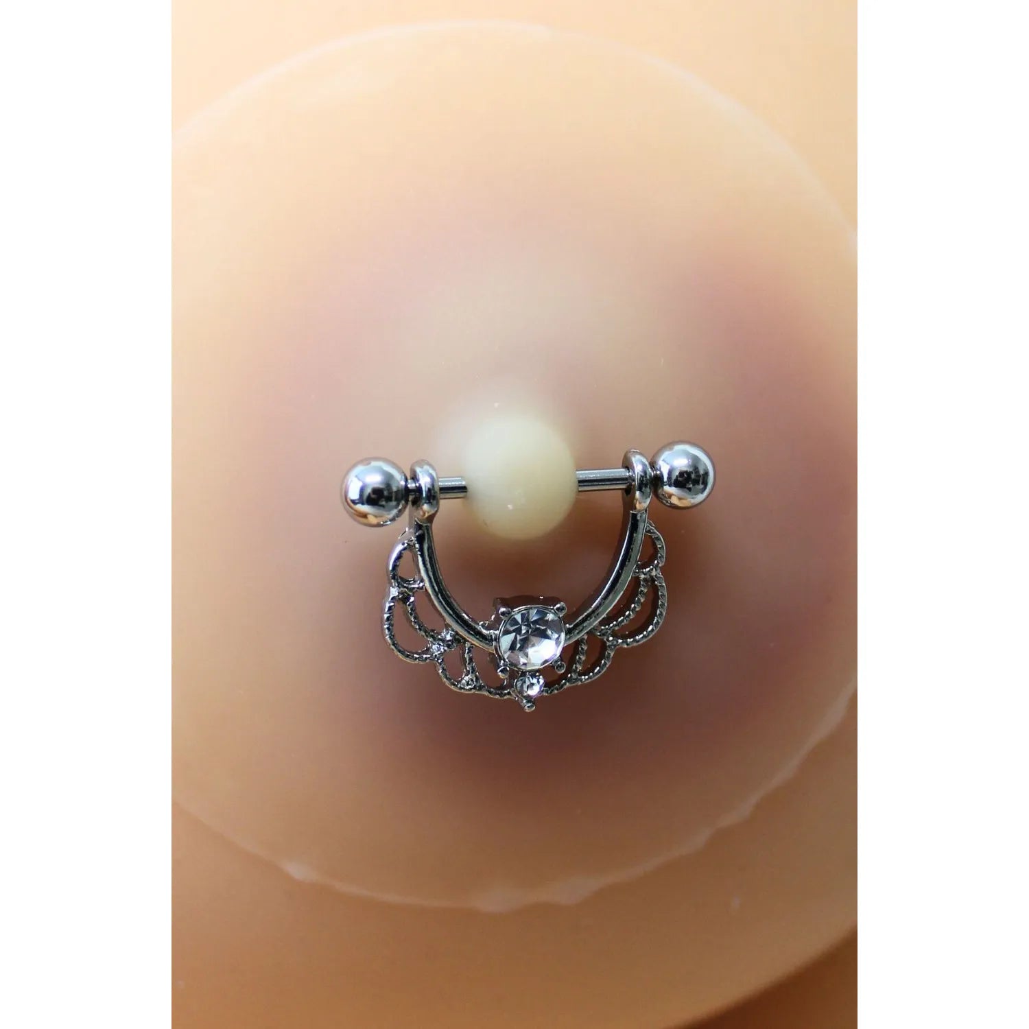 Cache-tétons silicone clair avec piercing demi-anneau strass, élégant et réutilisable pour peaux claires.