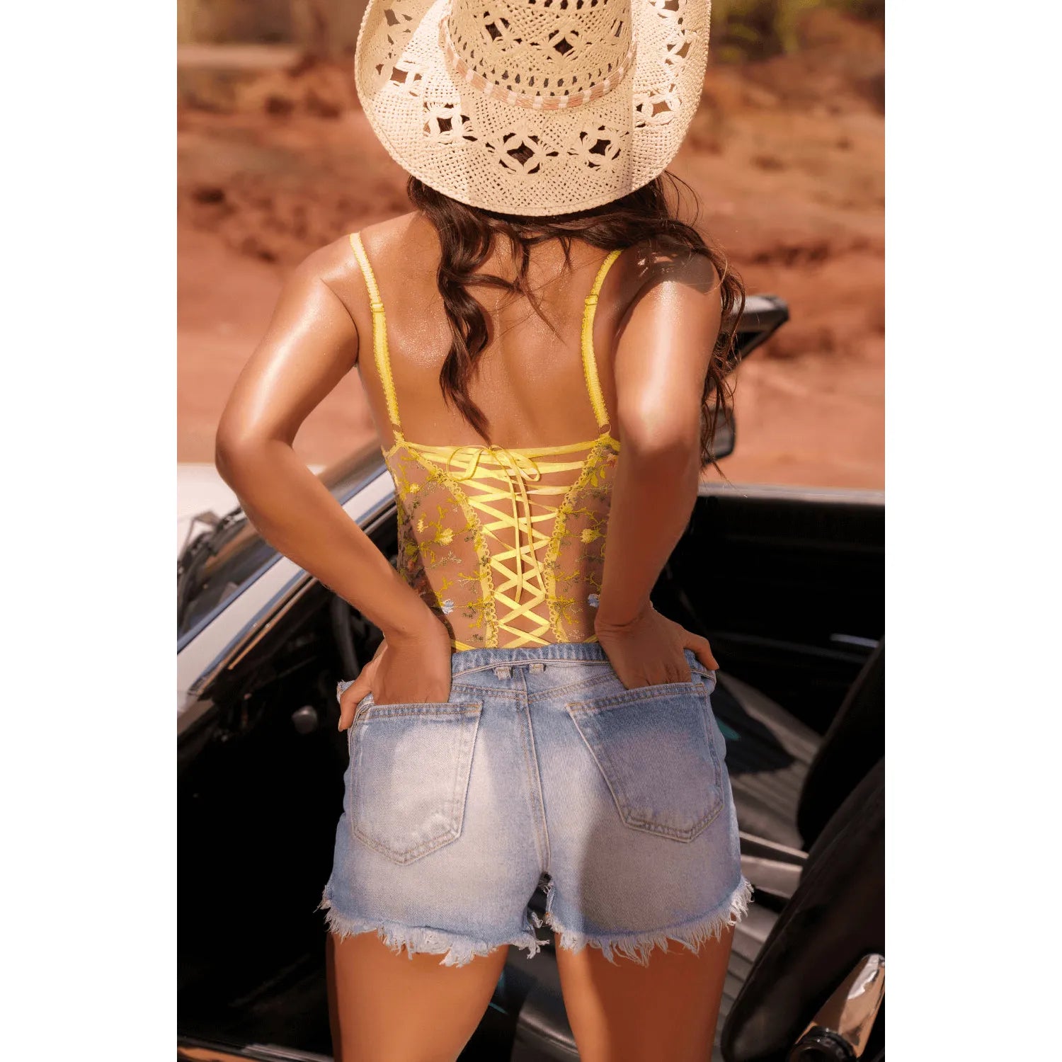 Body string jaune brodé fleurs, dos nu avec laçage croisé, bretelles réglables, porté avec short en jean, ambiance estivale.