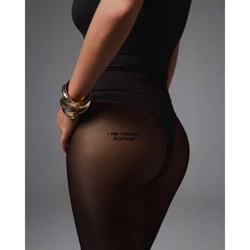 Collants noirs semi-transparents avec lettrage I am limited edition sur fond gris, portés par une femme élégante.