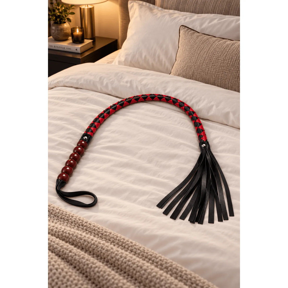 Fouet rouge et noir 80 cm en simili cuir, tressé avec lanières souples, sur lit beige, design élégant et robuste.