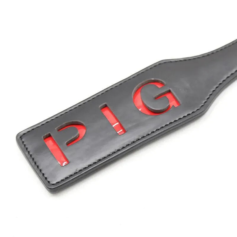 Paddle BDSM noir avec lettres découpées PIG en rouge, accessoire sans phtalates pour moments intimes.