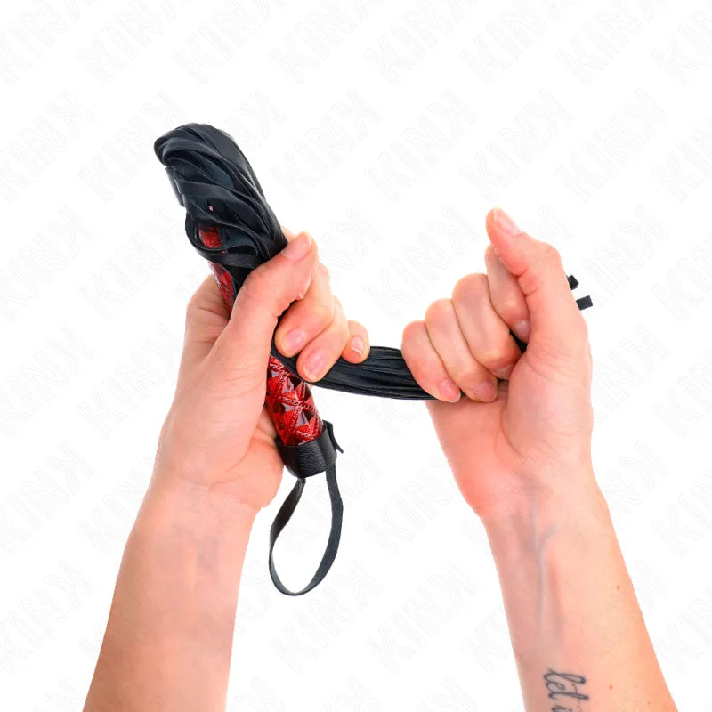Mains tenant un fouet BDSM rouge et noir en cuir véritable, accessoire de haute qualité pour plaisir raffiné.
