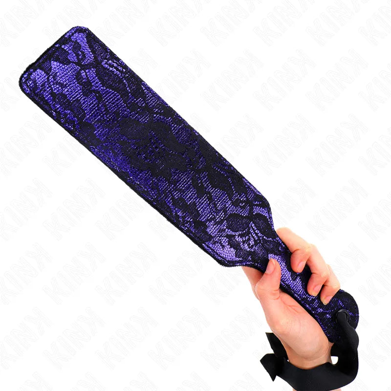 Accessoire BDSM en cuir haut de gamme, pagaie violette avec motif dentelle noire, tenue par une main.