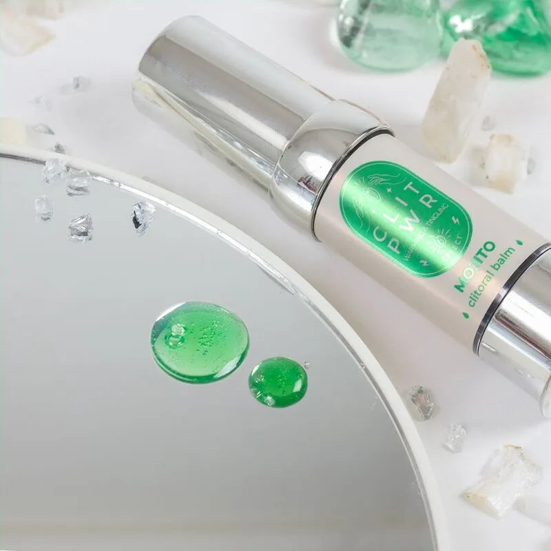 Flacon argenté de Baume Stimulant Clitoris Chauffant, avec étiquette verte, posé sur une surface réfléchissante.