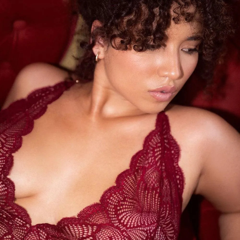 Body en dentelle ondulée bordeaux, dos ouvert, décolleté plongeant, porté par une femme sur fond rouge.