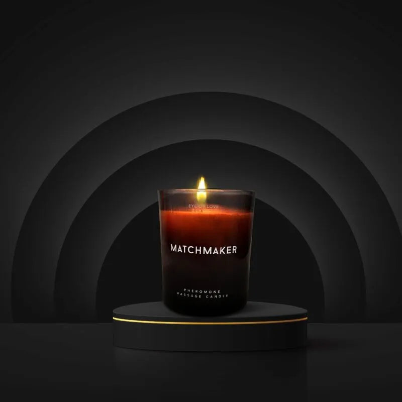Bougie de massage aux phéromones, cire rouge foncé, pot noir, flamme allumée, ambiance luxueuse et apaisante.