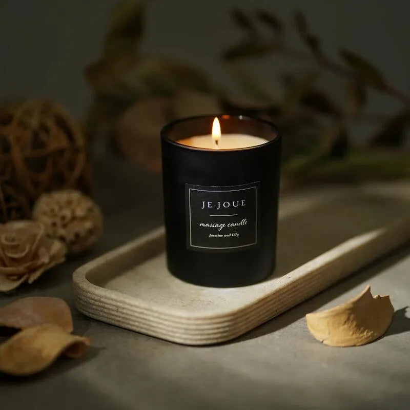 Bougie de massage noire allumée sur plateau, ambiance chaleureuse, parfums ylang ylang et mandarine, détente sensorielle.