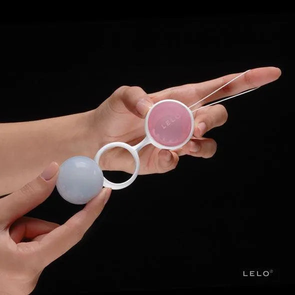 Boules Kegel ajustables roses et bleues pour renforcement pelvien post-partum, tenues dans une main sur fond noir.