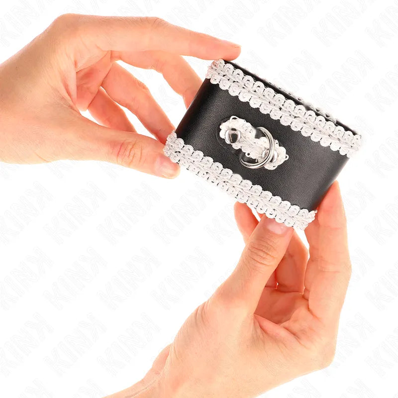 Bracelet BDSM en cuir vegan noir, bordé de dentelle blanche, avec boucle métallique, tenu par des mains.