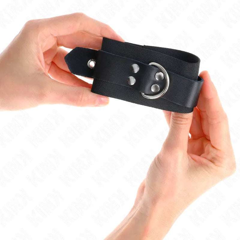 Bracelet BDSM en cuir végétalien noir, ajustable, avec boucle métallique, tenu par deux mains sur fond blanc.