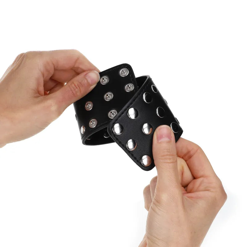 Bracelet BDSM noir en cuir végétalien avec rivets argentés, élégant et éthique, tenu par des mains sur fond blanc.