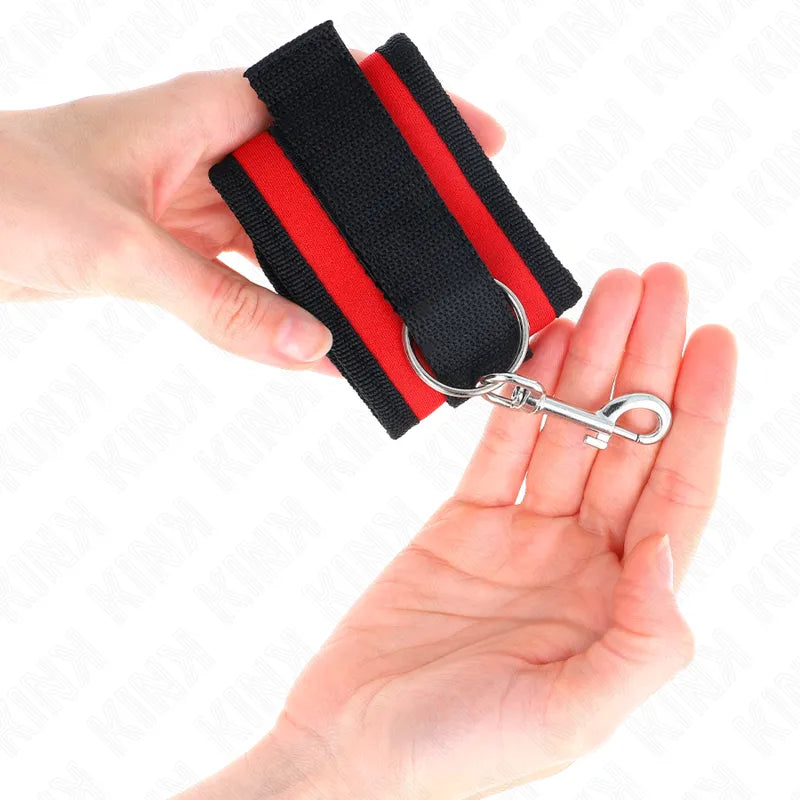 Bracelet BDSM en cuir végétalien noir et rouge, réglable, avec boucle métallique, tenu dans une main.