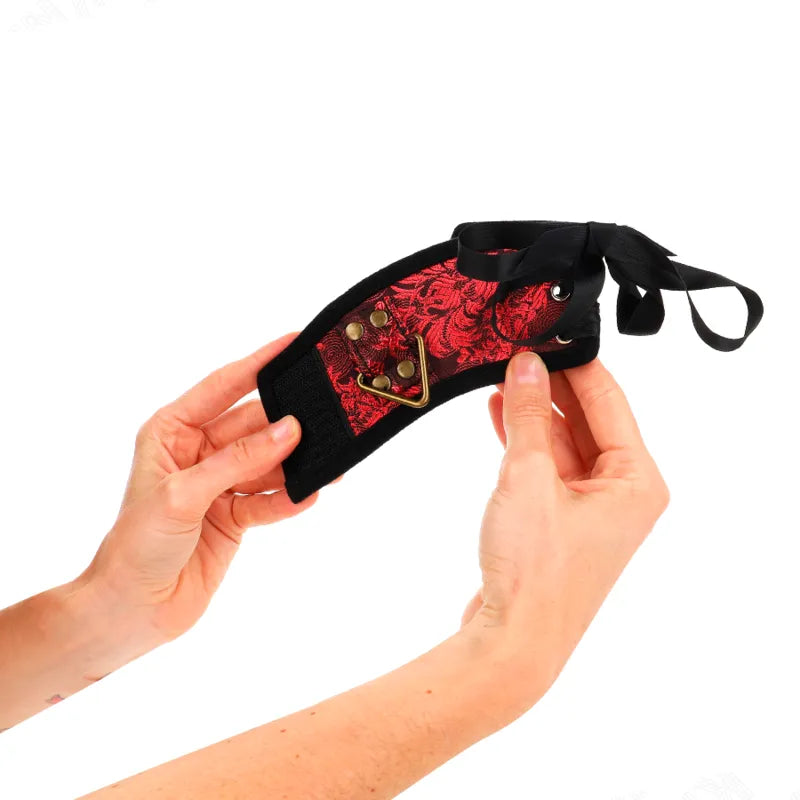 Bracelet BDSM en cuir noir et rouge, détails dorés, élégant et robuste, tenu par des mains, idéal pour sessions intenses.