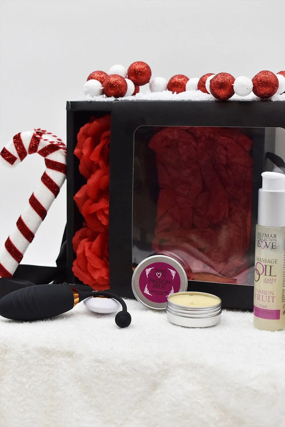 Coffret cadeau Noël noir avec huile et bougie de massage fruit de la passion, décorations rouges et blanches.