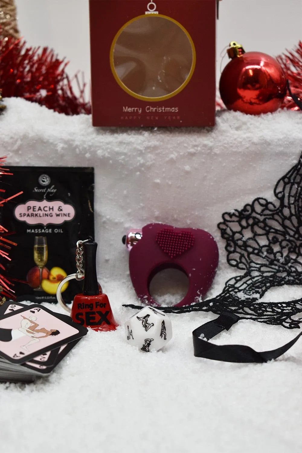 Coffret Coquin Noël avec huile de massage pêche, cockring cœur, accessoires sensuels sur fond festif enneigé.