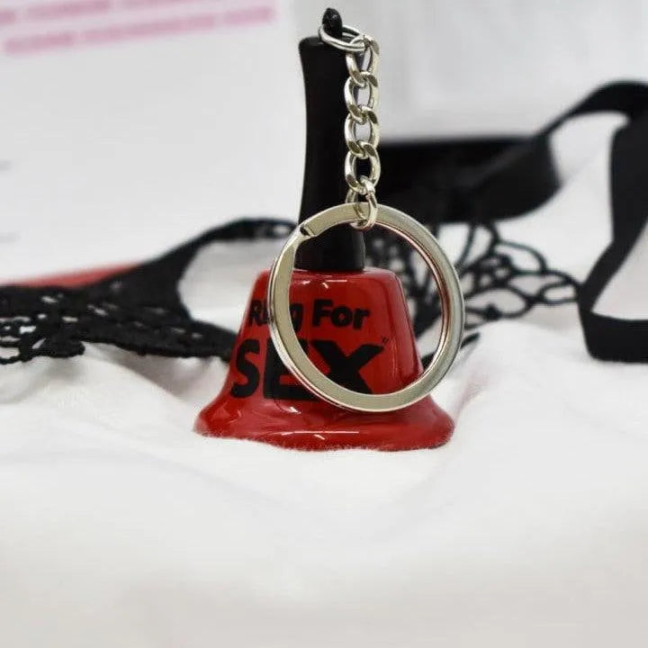 Coffret coquin édition limitée, cloche rouge et accessoires sensuels sur fond blanc, expérience intime pour couples.