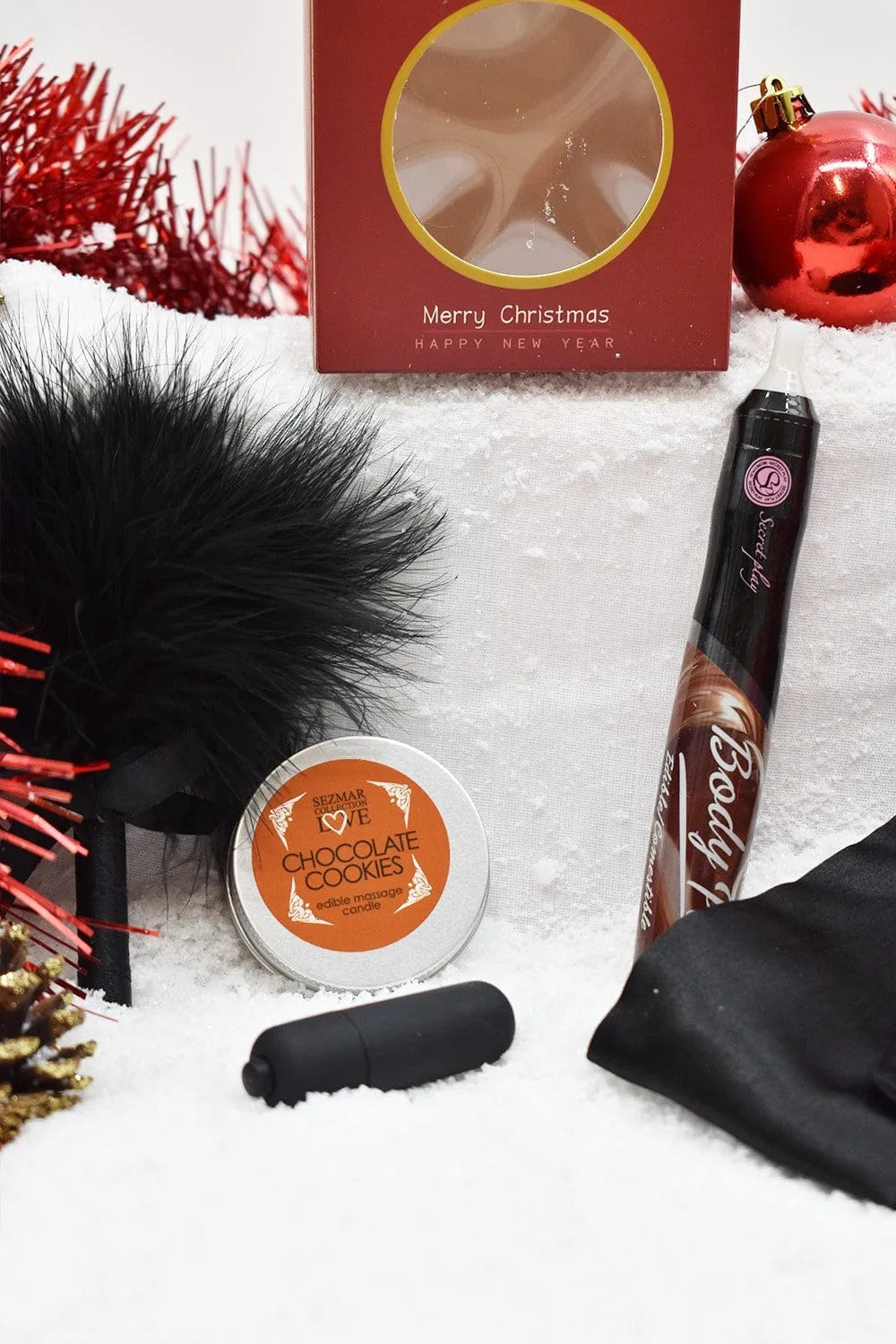 Coffret cadeau Noël chocolaté avec accessoires sensuels, boîte rouge, flacon, plume noire et décorations festives.