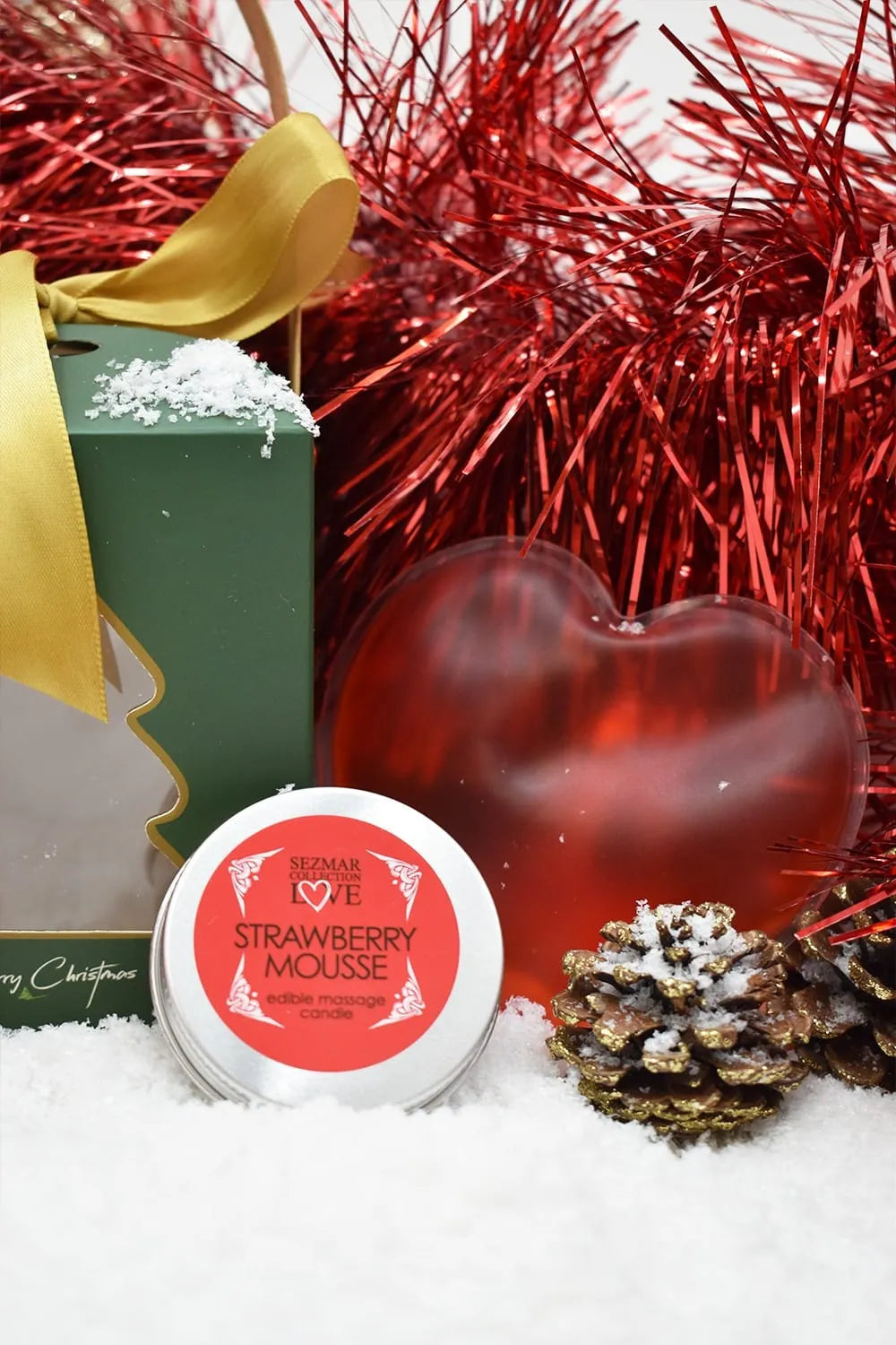 Coffret massage Noël avec huile fraise, cœur chauffant rouge, bougie et pétales, décor festif rouge et or.