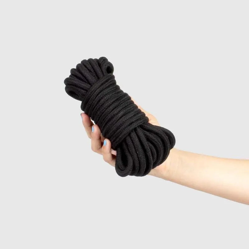 Corde shibari noire soyeuse pour bondage BDSM, enroulée, tenue dans une main, idéale pour expérience sensuelle sécurisée.