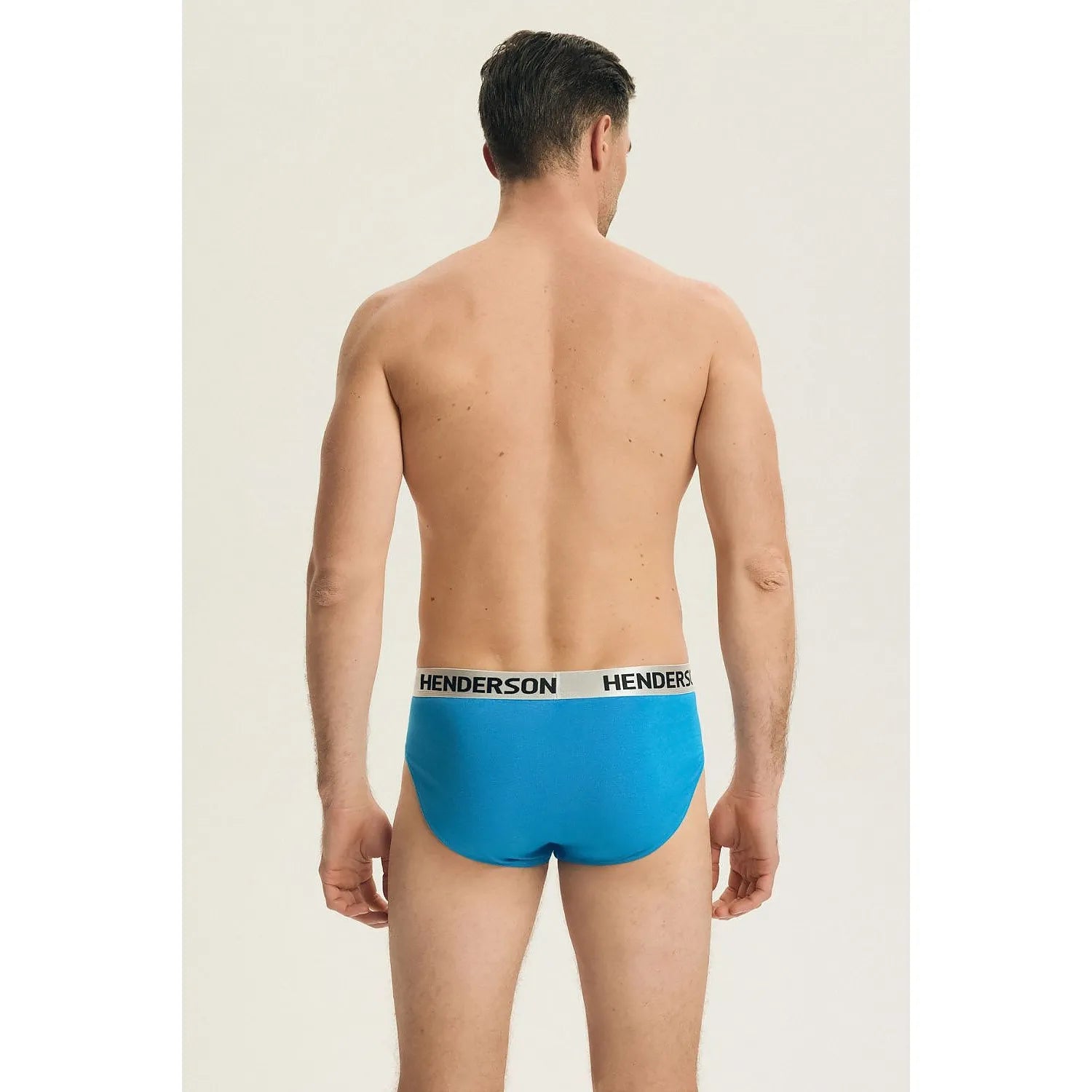 Homme portant un slip bleu en coton Henderson 224350, coupe ajustée, ceinture élastique blanche avec logo Henderson.