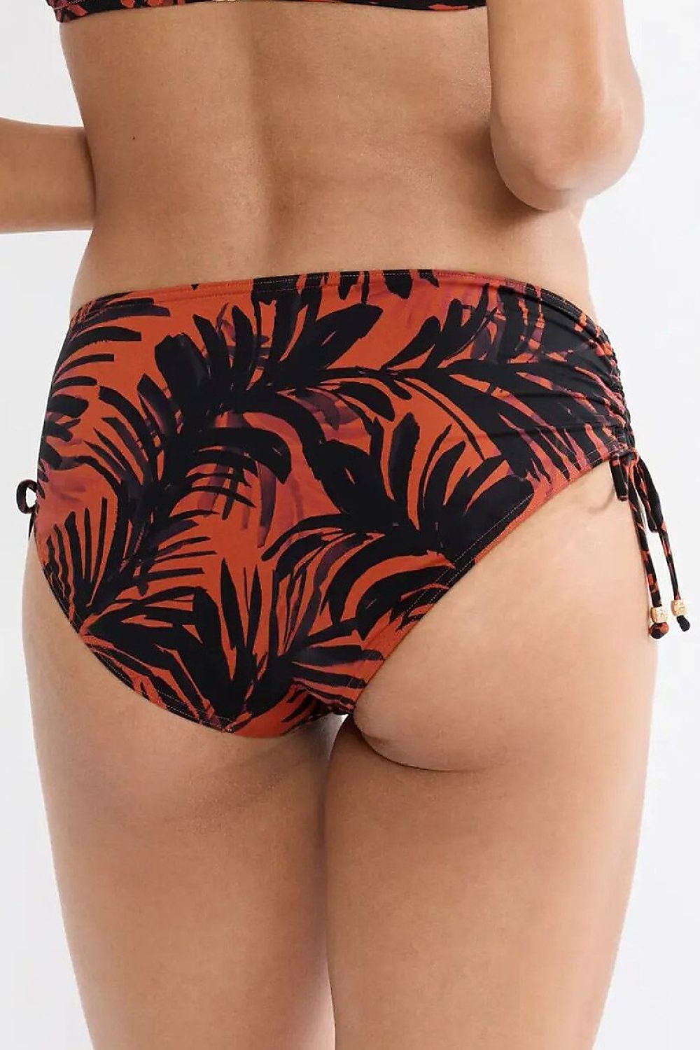 Culotte bikini Triumph Summer Palm, motif feuilles noires sur fond orange, côtés réglables, détails métalliques.