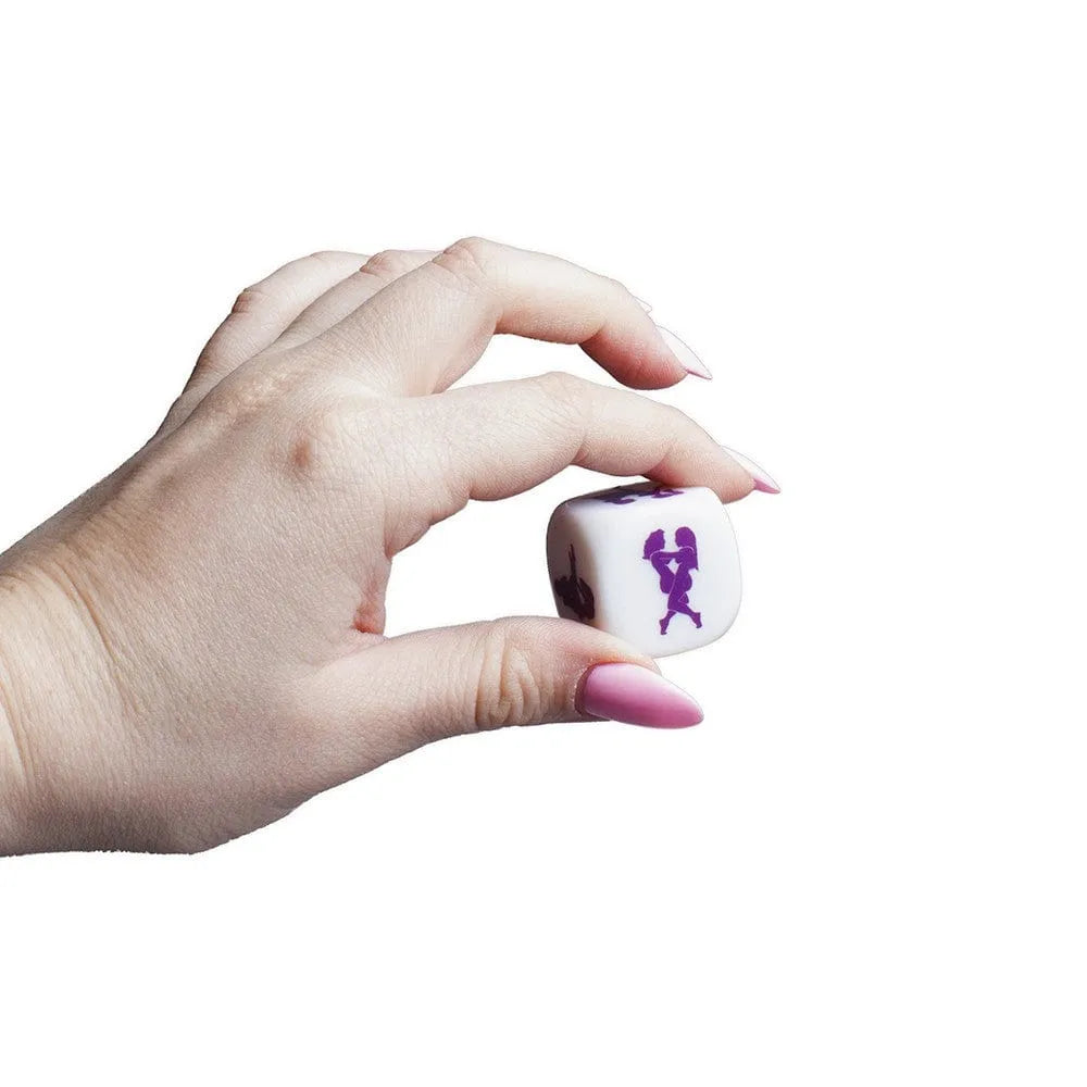 Dé Kamasutra blanc 2,5 cm avec illustrations violettes, tenu par une main, pour explorer des positions érotiques en couple.