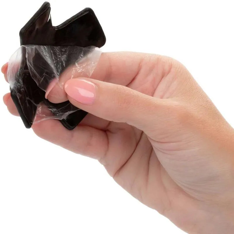 Cache-tétons noir en forme de croix avec joint torique, détails métalliques, tenu par une main, design élégant et réutilis...