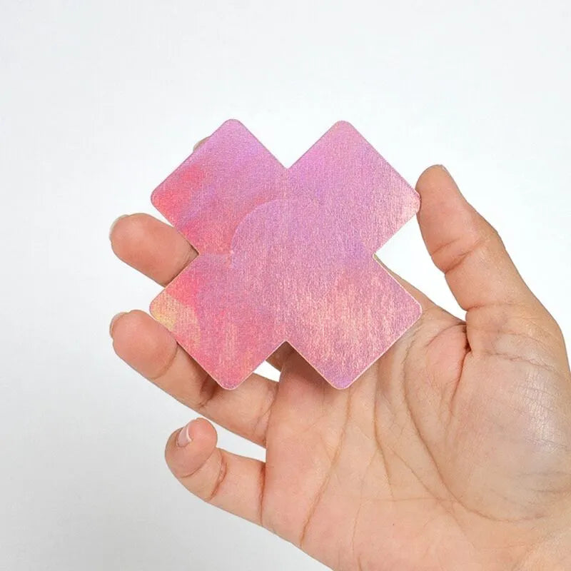 Cache-tétons holographiques noir rose en forme de croix, tenus dans une main, parfaits pour soirées et festivals.