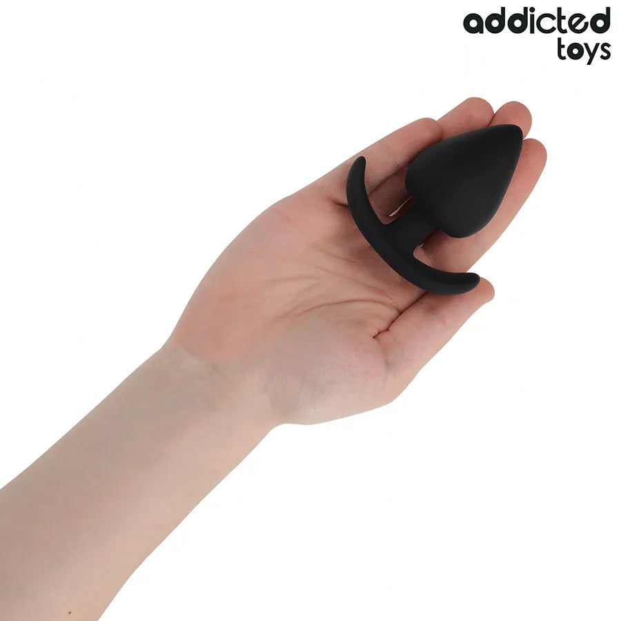 Plug anal noir Addicted Toys XL, forme conique, base élargie en T, silicone hypoallergénique, dans une main.