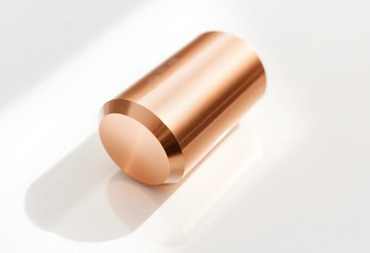 Dispositif cylindrique en cuivre posé sur une surface blanche