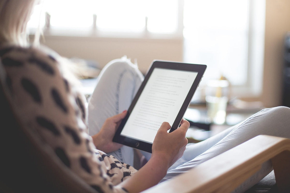 Femme lisant un livre numérique sur une tablette dans son salon