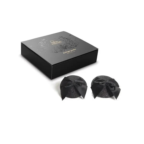 Cache-tétons noirs pailletés avec nœuds satin, style burlesque, élégance et sensualité, boîte Bijoux Indiscrets.