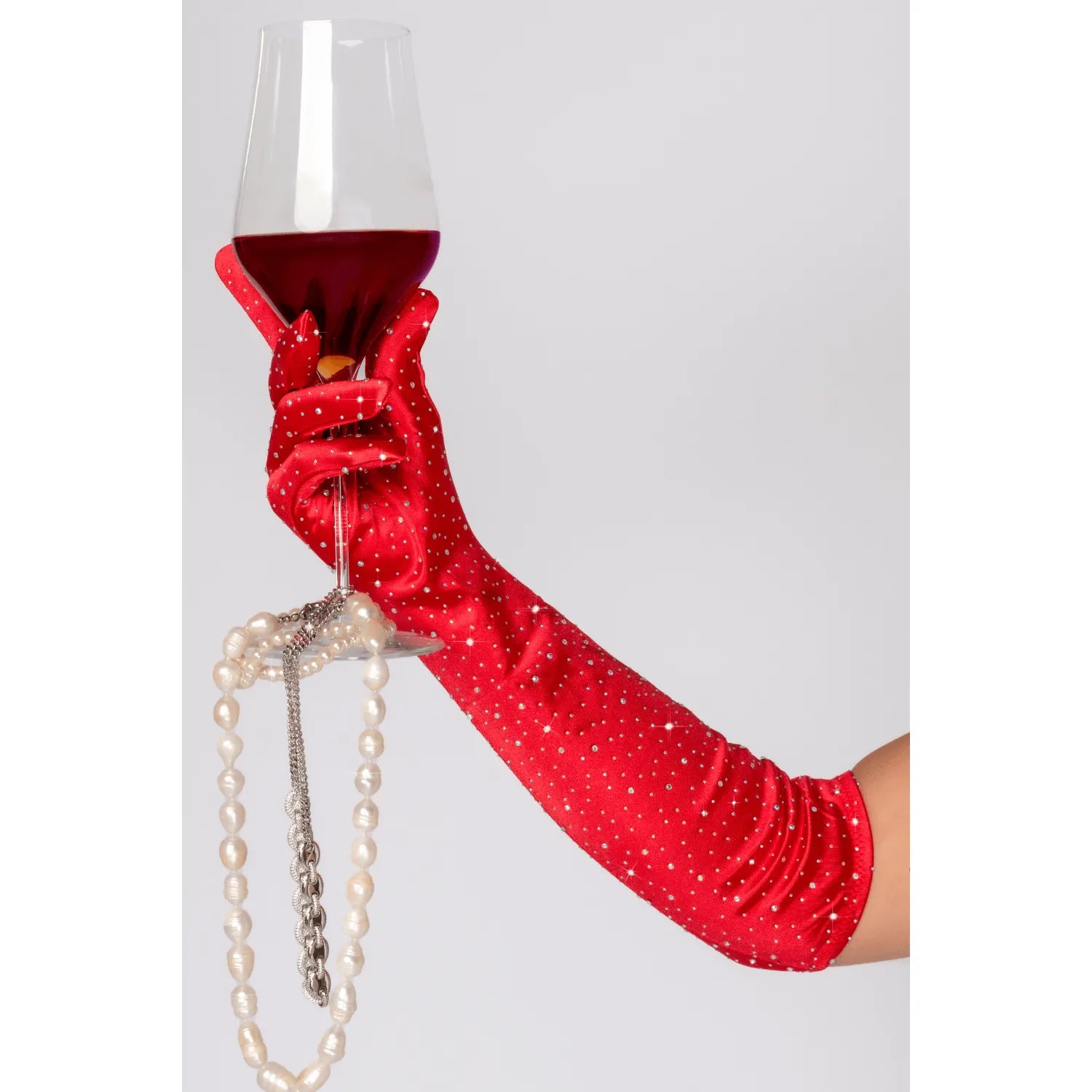 Gant opéra rouge satin extensible avec strass, main tenant un verre de vin et collier de perles, chic et élégant.