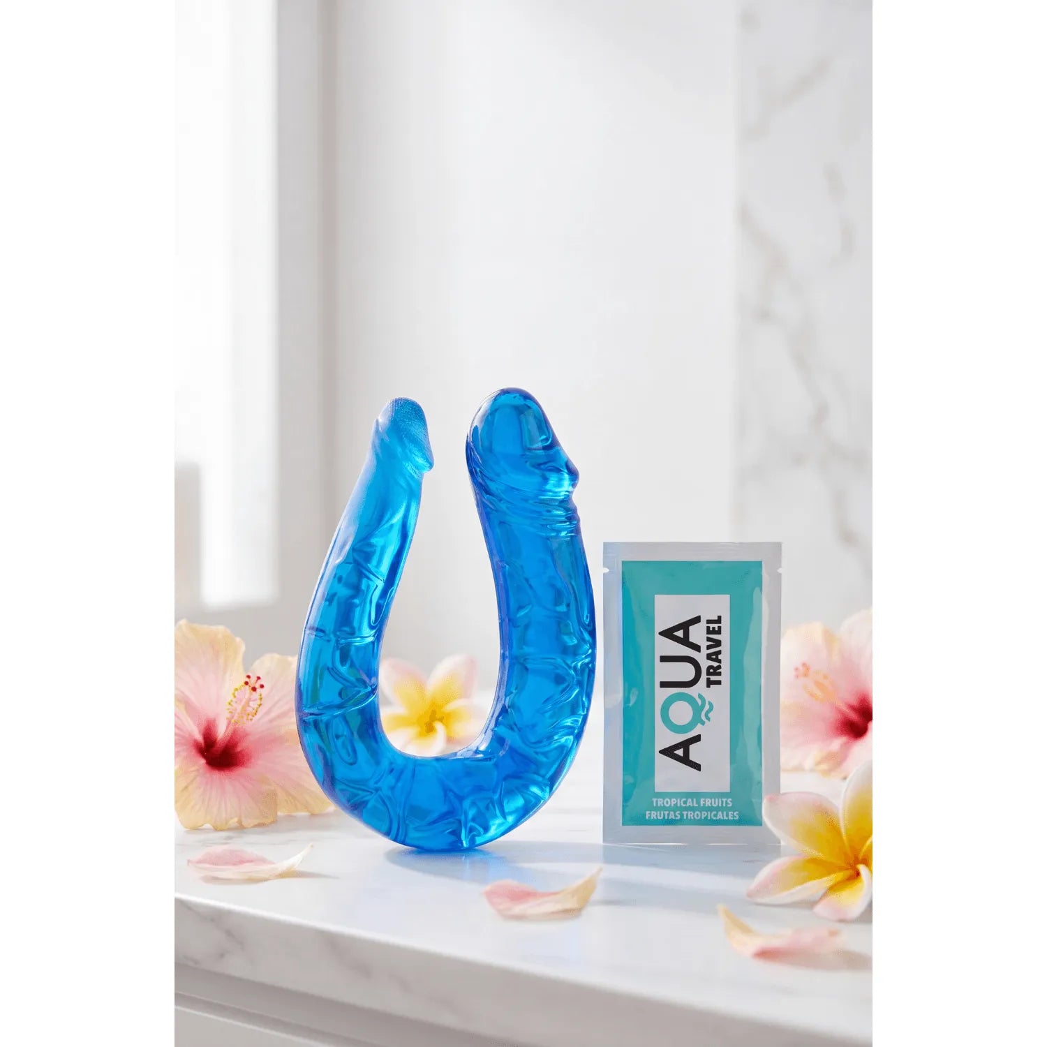 Double dong bleu flexible en TPE avec reliefs réalistes, accompagné d'une dosette de lubrifiant, sur fond floral.