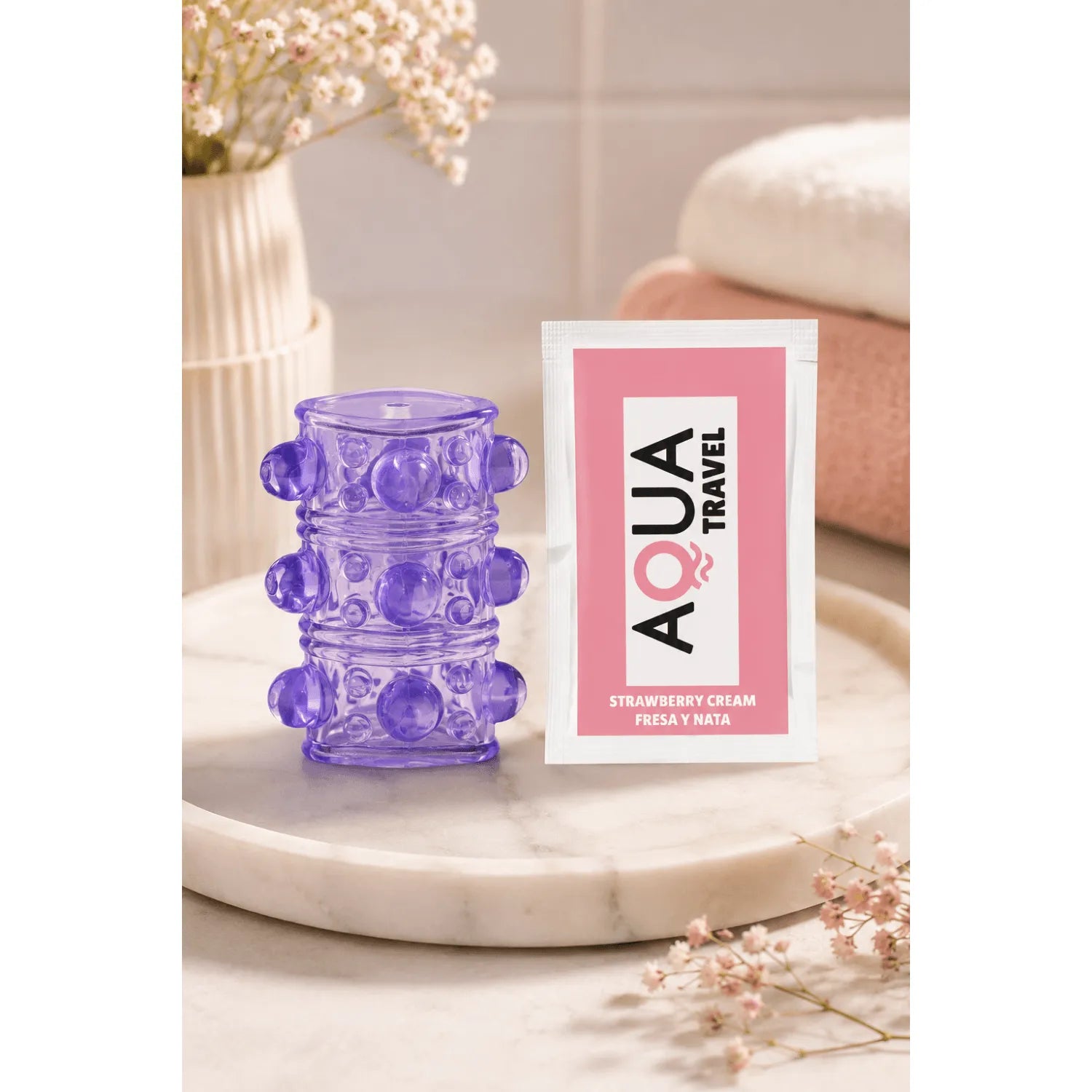 Gaine pénienne violette ultra-extensible avec picots et reliefs, posée sur une surface, à côté d'un sachet Aqua Travel.