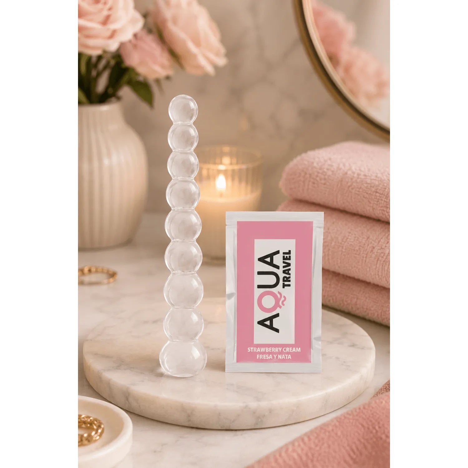 Chapelet anal en verre transparent, neuf boules progressives, sur fond de salle de bain élégante avec serviettes roses.
