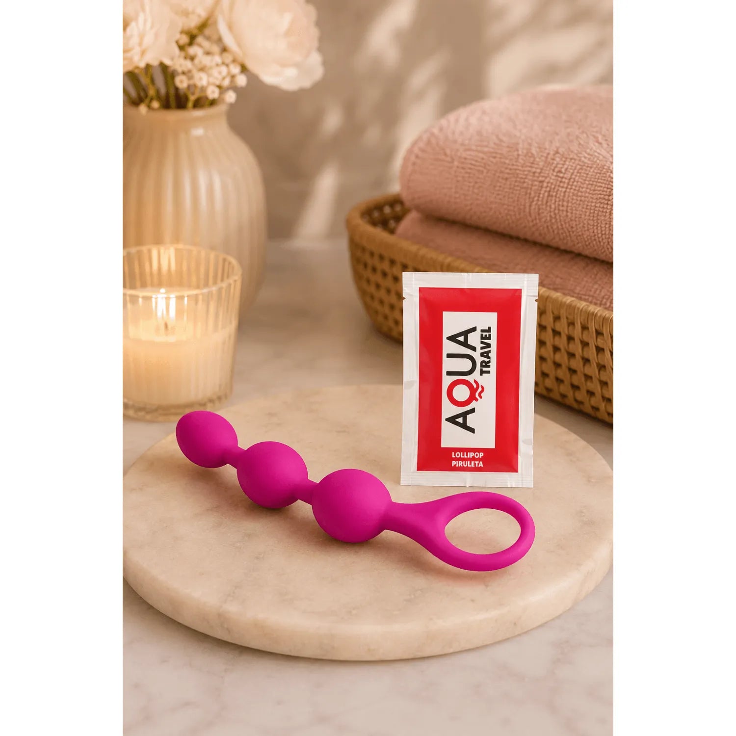 Chapelet anal 3 boules silicone fuchsia progressif, ergonomique, sur table avec bougie et serviettes, idéal débutants.