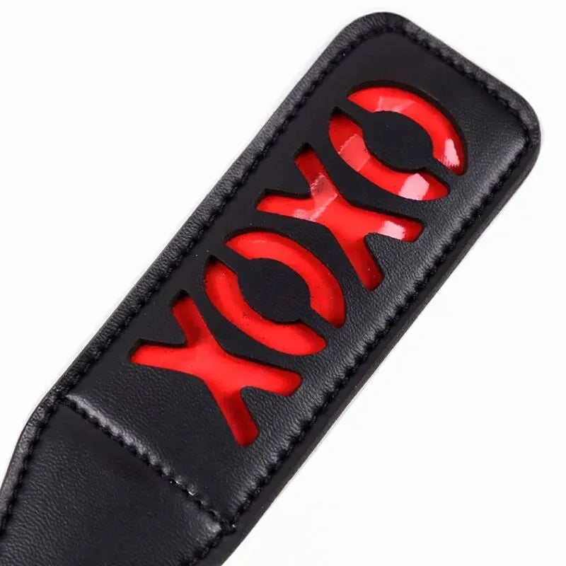 Pagaie BDSM noire avec découpe XOXO rouge, design élégant et sécuritaire pour jeux sensuels.