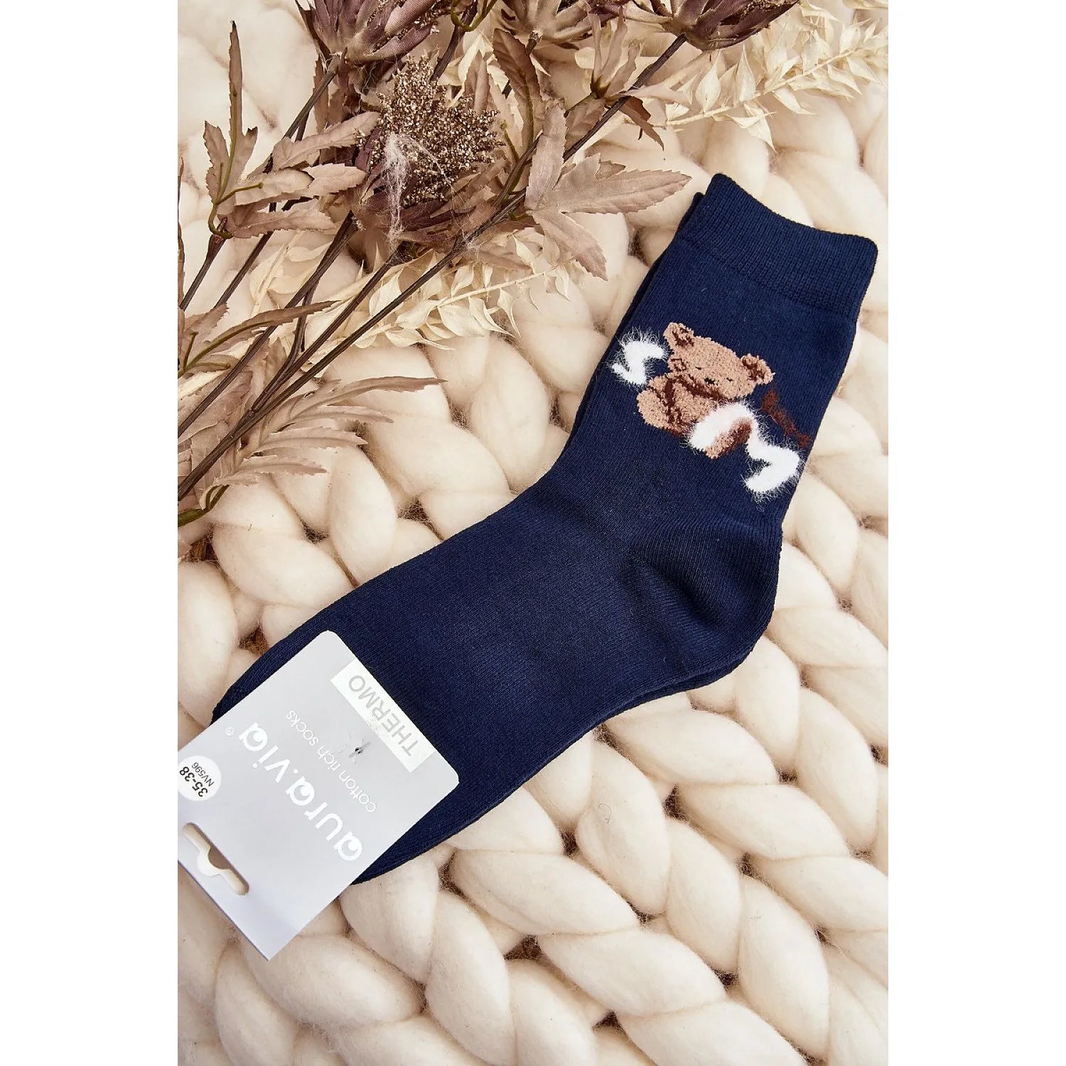 Chaussettes bleues en coton avec patch ourson, idéales pour journées froides, posées sur fond tricoté beige.