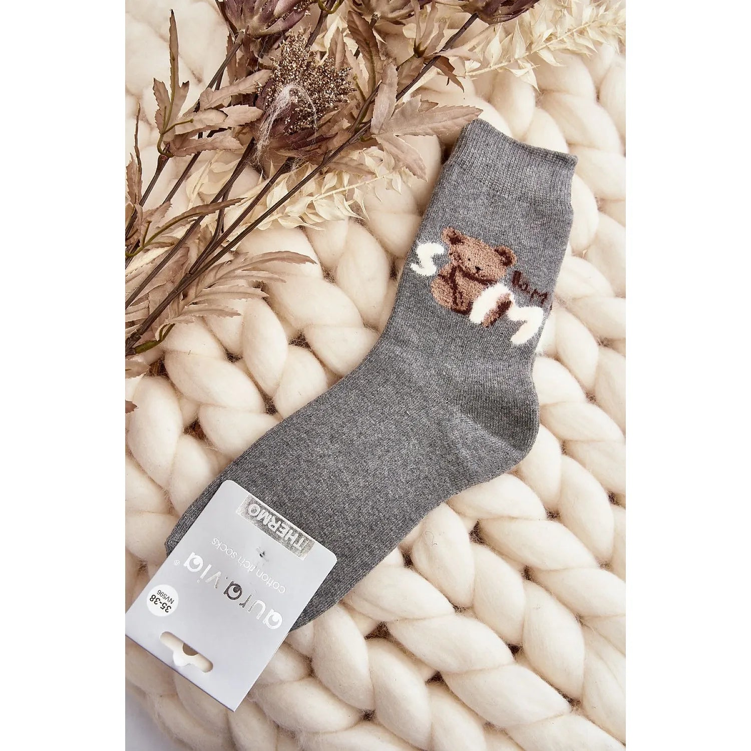 Chaussettes grises en coton avec patch ourson, idéales pour l'hiver, posées sur un fond de laine tressée et fleurs séchées.