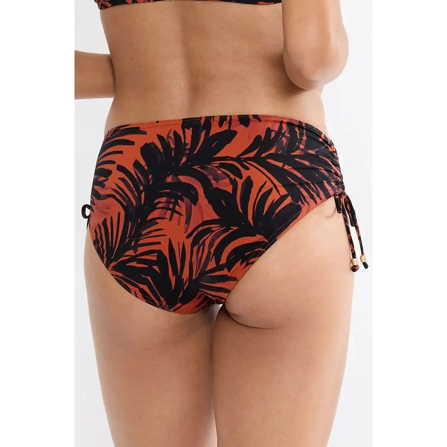 Culotte bikini Triumph Summer Palm, motif feuilles noires sur fond orange, côtés réglables, détails métalliques.