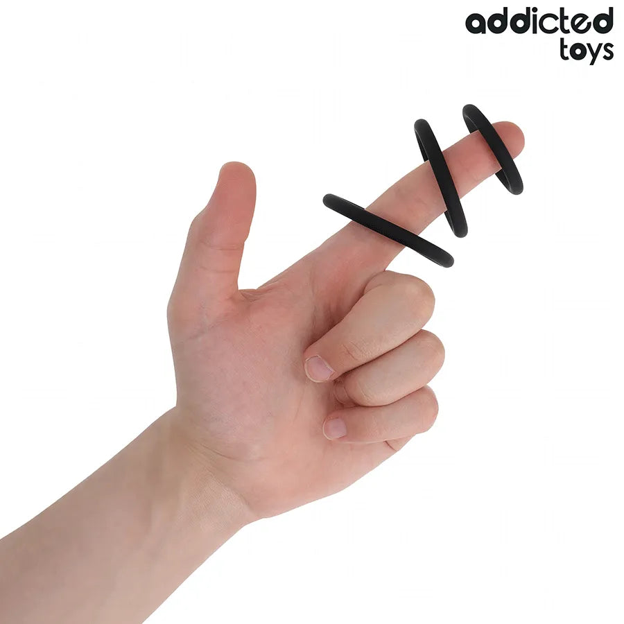 Anneaux péniens en silicone noir Addicted Toys sur doigt, trois tailles pour stimulation et confort optimisés.