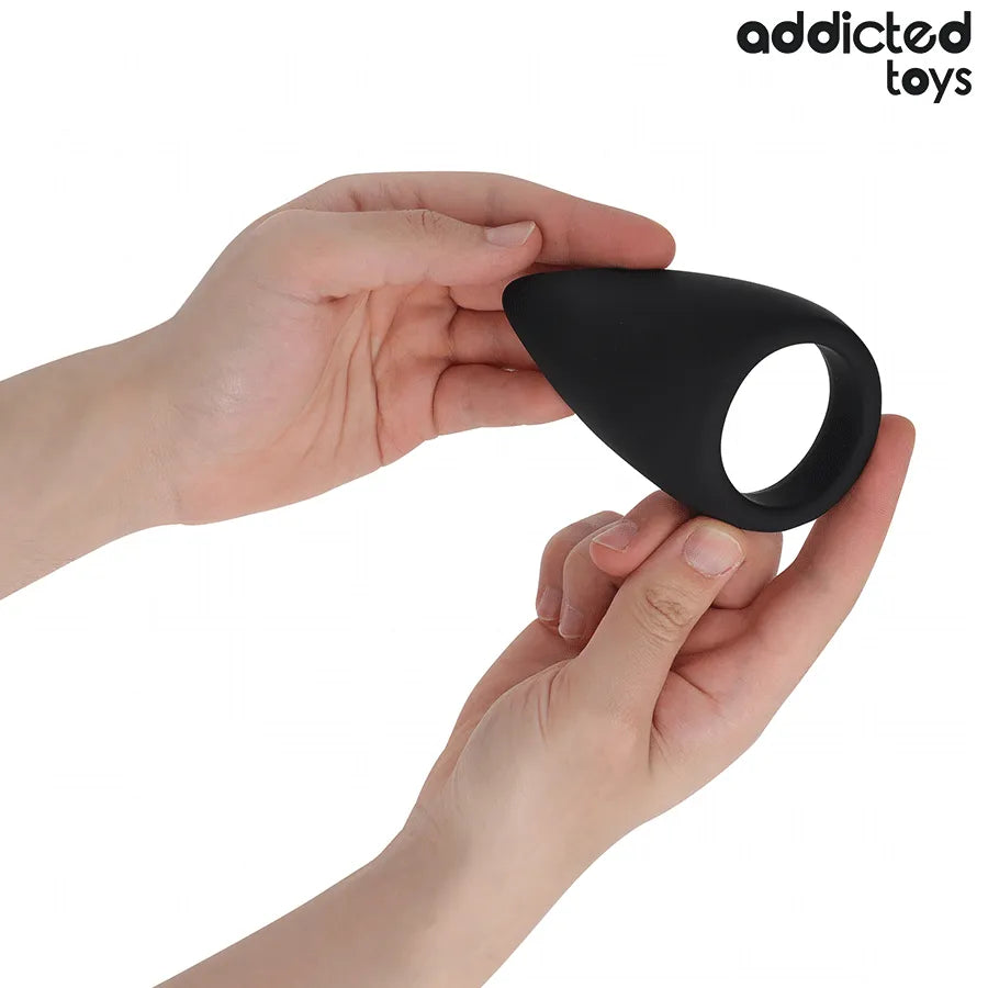 Anneau pénien noir en silicone, forme de larme, tenu par des mains, améliore l'érection, Addicted Toys.