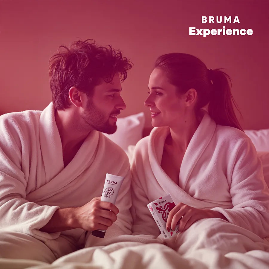 Duo en peignoirs blancs avec kit BRUMA XPERIENCE, produits aux couleurs vives, ambiance intime et ludique.